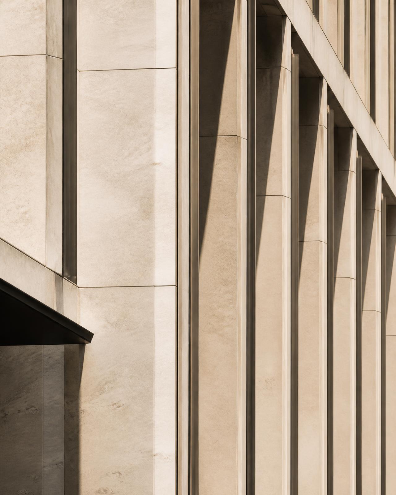 Detail of a modern commercial building facade in warm stone with fine vertical mullions